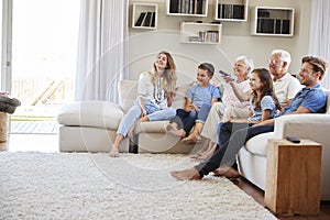 Multi Generation Family Sitting On Sofa At Home Watching TV