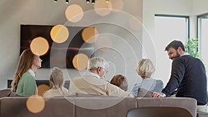 Multi generation family sitting together on sofa at home and watching TV