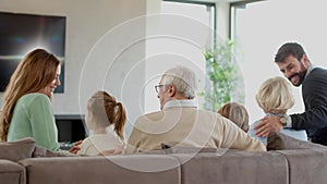 Multi generation family sitting together on sofa at home and watching TV