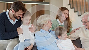 Multi generation family sitting together on sofa at home and watching TV