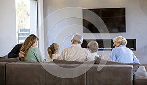 Multi generation family sitting together on the sofa at home and watching TV