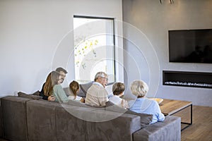 Multi generation family sitting together on the sofa at home and watching TV