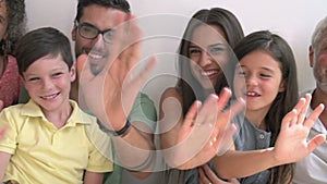 Multi Generation Family Standing Against Wall And Waving