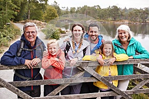 Multi generation family standing behind a wooden fence looking to camera, Lake District, UK