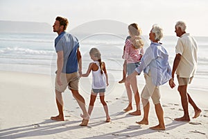 Multi Generation Family On Vacation Walking Along Beach Together