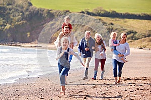 Multi-Generation Family Walking Along Shoreline Of Beach By Waves Together