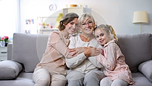 Multi-generation females hugging on home sofa smiling camera, family closeness photo