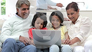 Multi-Generation Indian Family With Laptop Sitting On Sofa