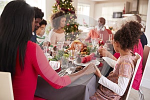 Multi generation, mixed race family holding hands and saying grace at the Christmas dinner table, side view