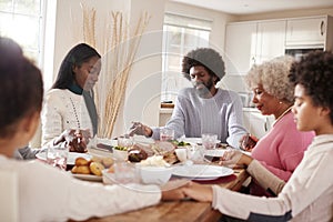 Multi generation mixed race family holding hands and saying grace before eating their Sunday dinner