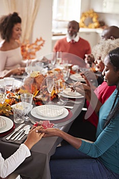 Multi generation mixed race family holding hands and saying grace before eating at their Thanksgiving dinner table, selective focu