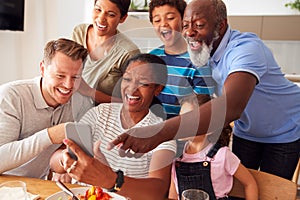 Multi-Generation Mixed Race Family Posing For Selfie As They Eat Meal Around Table At Home Together