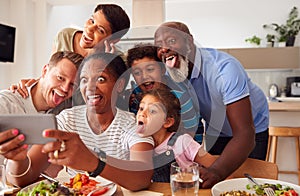 Multi-Generation Mixed Race Family Posing For Selfie As They Eat Meal Around Table At Home Together