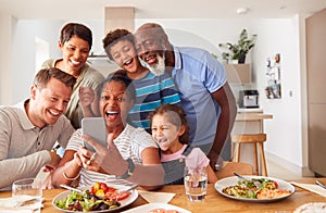 Multi-Generation Mixed Race Family Posing For Selfie As They Eat Meal Around Table At Home Together
