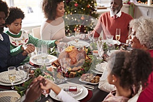 Multi generation mixed race family sitting at Christmas dinner table holding hands and saying grace, elevated view