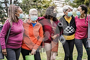 Multi generational women having fun before yoga class wearing safety masks at park outdoor - Main focus on right girl face