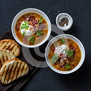 Multi grain and vegetables soup with grilled cheese sandwiches and crispy bacon on a dark background, top view. Delicious comfort