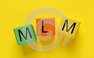 Multi-level marketing. Abbreviation MLM of cubes with letters on yellow background, top view