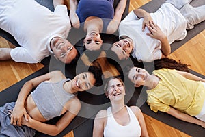 Multi-racial smiling people lie on mats after doing yoga at a fitness club. A group of young athletes relax and rest after