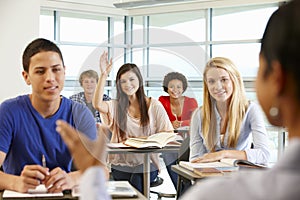 Multi racial teenage pupils in class one with hand up