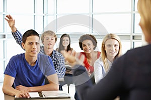 Multi racial teenage pupils in class one with hand up