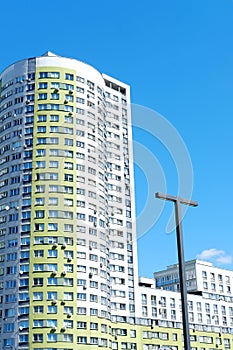 Multi-storey building in the form of a cylinder and painted in white and green colors against a blue sky.