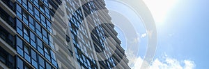 Multi-storey building with many glass windows standing against background of blue sky and sun