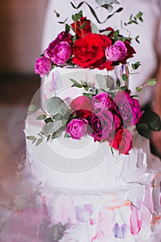 Multi tiered beautiful wedding cake with white cream decorated with pink and red roses and eucalyptus