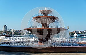 Multi-tiered musical singing fountain against white arch. Pool and bowls of fountain are made of red granite on embankment