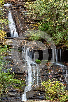 Multi tiered waterfall across wet rocks covered in autumn leaves and moss
