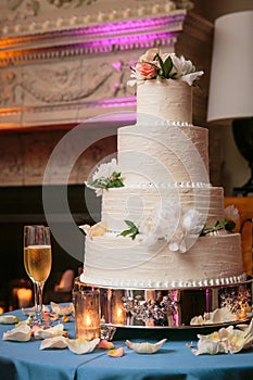 Multi tiered wedding cake with white flowers and cream frosting on a table with candles and champagne glasses - wedding cake