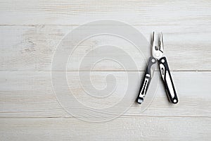 Multi tool with black handles on a white wooden background. Top view of desktop