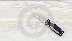 Multi tool with black handles on a white wooden background. Top view of desktop