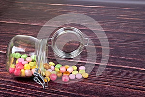 Multicolor candies in a glass jar on a wooden background