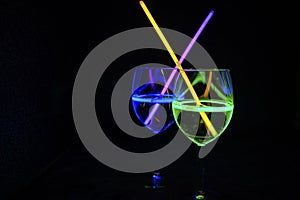 Multicolor Cocktail wine glass filled with illuminated relaxing alcohol drink and colorful straw with black background for