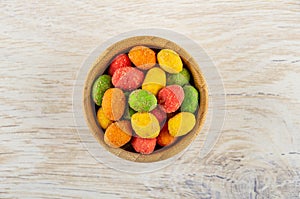 Multicolor dragee with peanut in bowl on wooden table. Top view