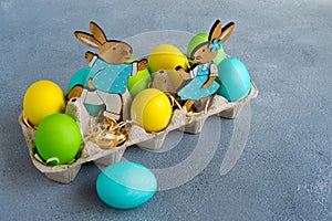 Multicolor easter eggs with easter bunnies in egg carton on grey background