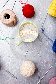 Multicolor knitting ball and needles around green cup of coffee on grey background. Top view. Copy space. Knitting yarn.