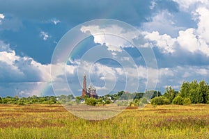 Multicolor rainbow on the background of a beautiful cloudy sky and a red church with a bell tower