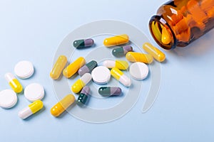Multicolor tablets and pills capsules from glass bottle on blue background Close-up