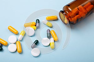 Multicolor tablets and pills capsules from glass bottle on blue background Close-up