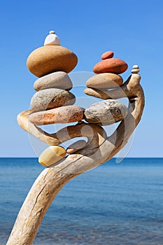 Multicolored balanced stones on an wooden snags, on a blue sky and sea background