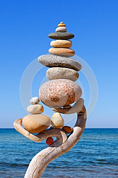 Multicolored balanced stones on an wooden snags, on a blue sky and sea background. Concept of balance