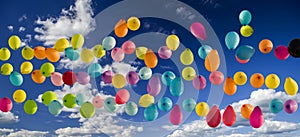 Multicolored balloons soar into the sky. Against the blue sky with white clouds