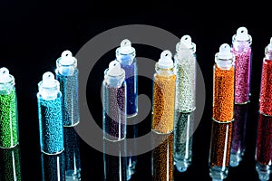 Multicolored beads in bottles for the design of nails on a black background