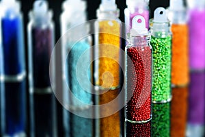 Multicolored beads in bottles for the design of nails on a black mirror background