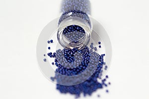 Multicolored beads in glass jars. Beads are poured on a white background. Plastic multi-colored polymers. Plastic pillets