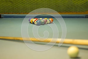 A multicolored billiard balls with numbers lie in the shape of a pyramid on a table with a blue cloth against the background of a