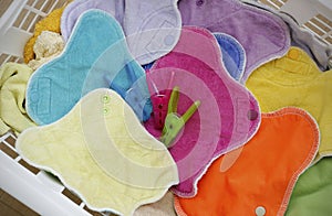 Multicolored clean cloth menstrual pads and three clothespins inside a white laundry basket