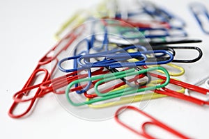 Multicolored colorful paper clips on a white table background close up